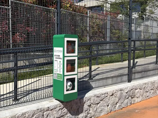 Zeleni Unlokie ormarić postavljen uz ogradu igrališta, na kamenom zidu, po jakom suncu